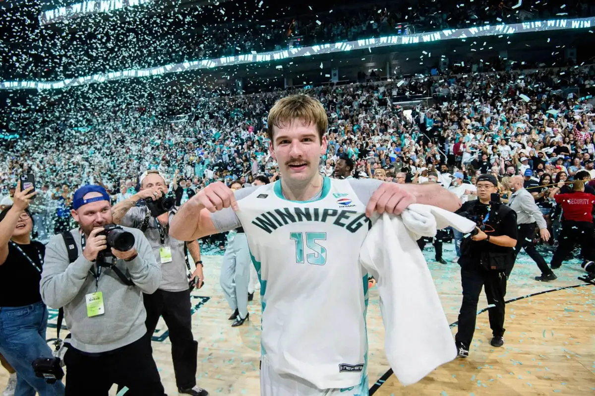 Simon Hildebrandt points to the Winnipeg Sea Bears logo on his jersey as photographers capture the moment and confetti falls from the rafters after his game-winning three-pointer gave Winnipeg its first CEBL championship.